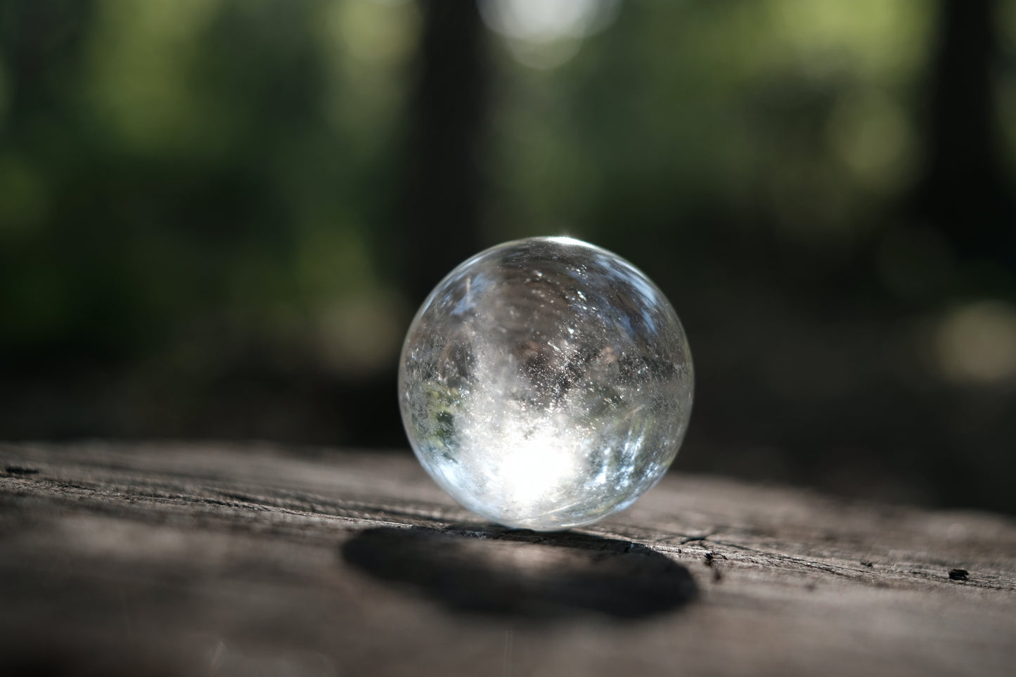 Clear quartz ball shown with sunbeams on a tree stump in the woods.