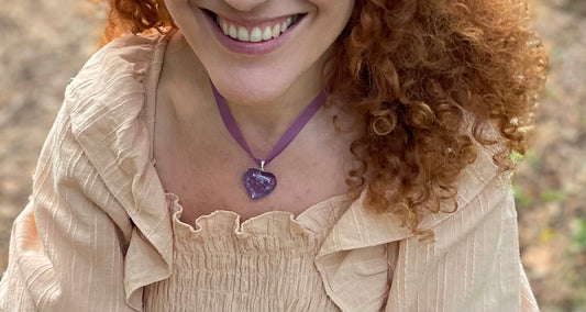 Purple heart shaped Amethyst pendant threaded on purple ribbon. It is worn on a girl's neck.