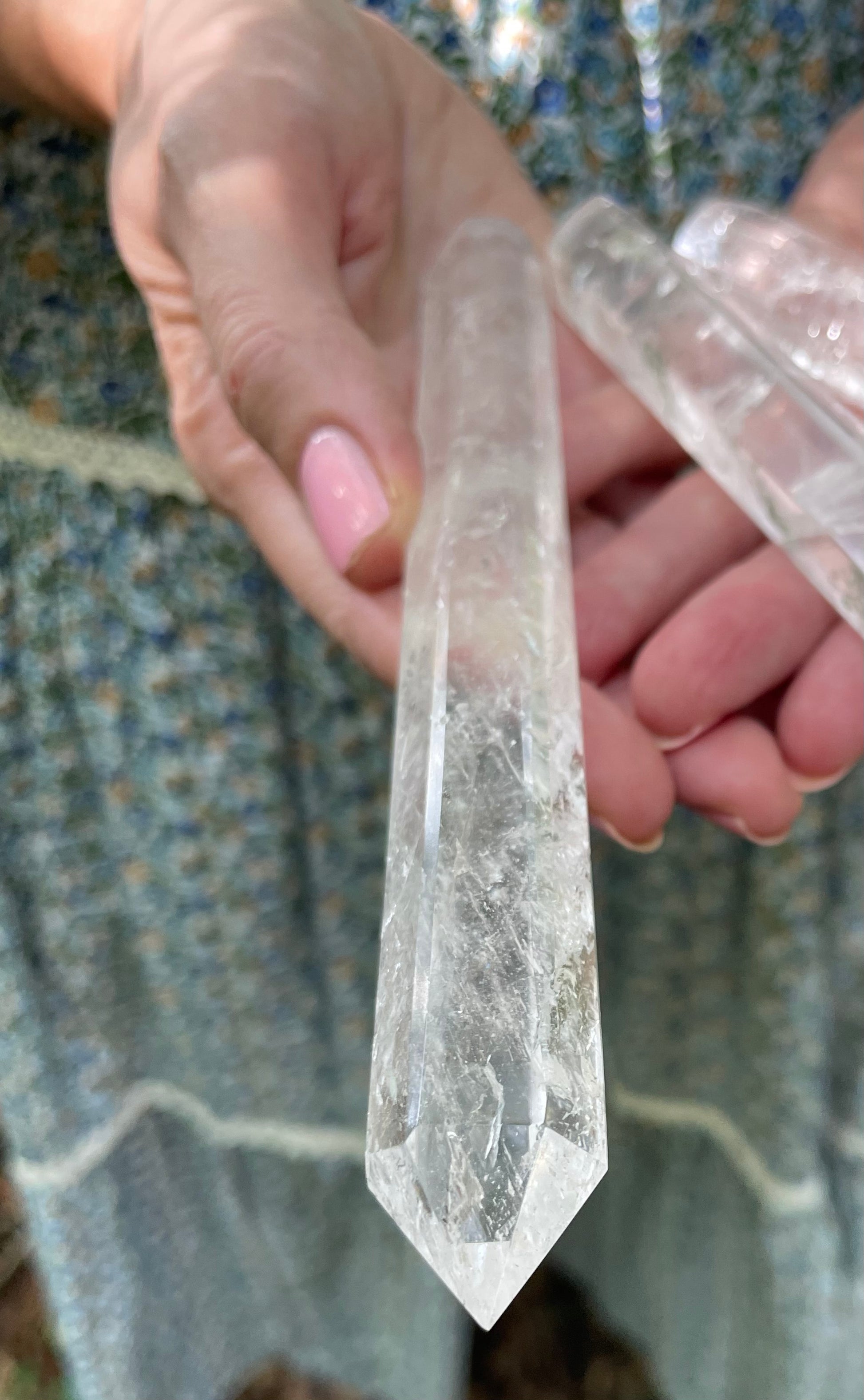 Three clear crystal wands shown in three sizes. Held in models hand showing her blue floral skirt. The background is the forest.