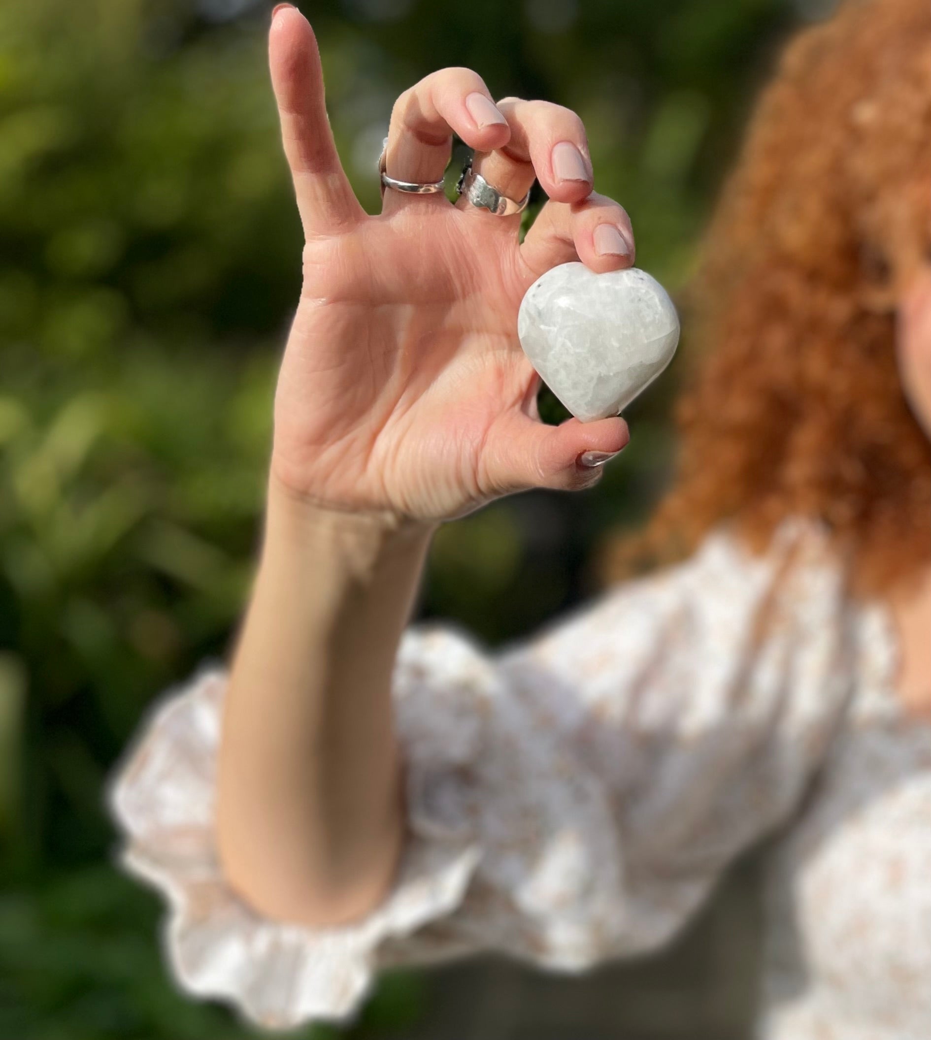 Polished white moonstone heart crystal in models hand with red hair and frilly top