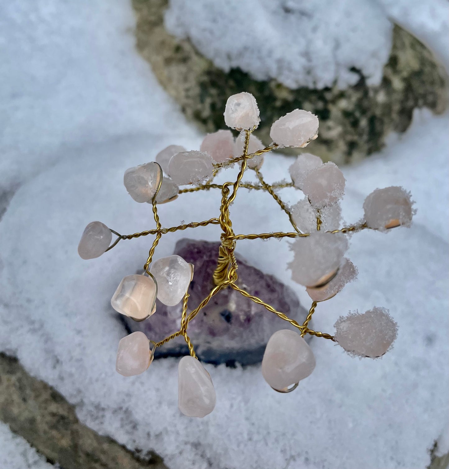 Rose quartz and amethyst crystal tree photographed in the snow