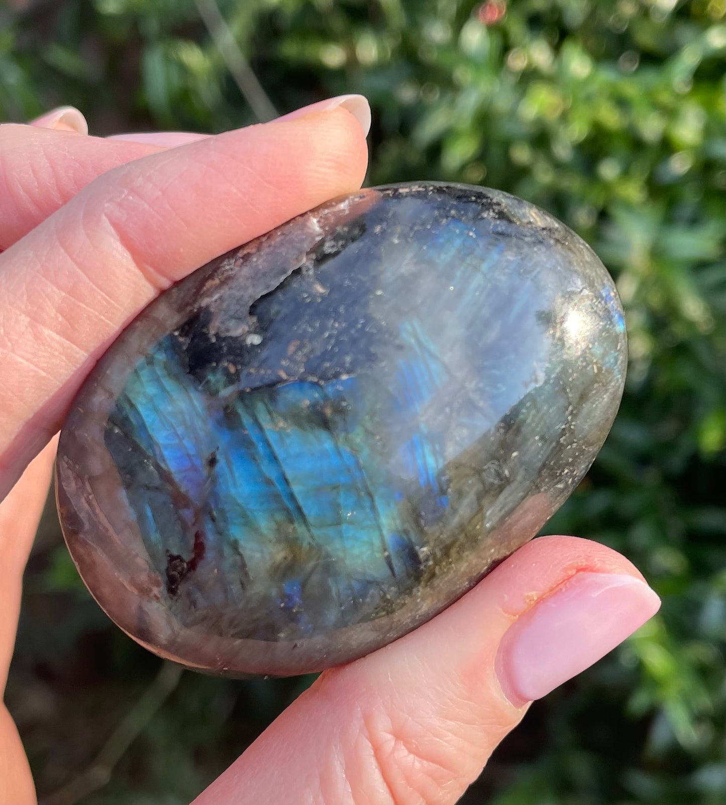 Heart shaped polished labradorite photographed in models hand in the woods