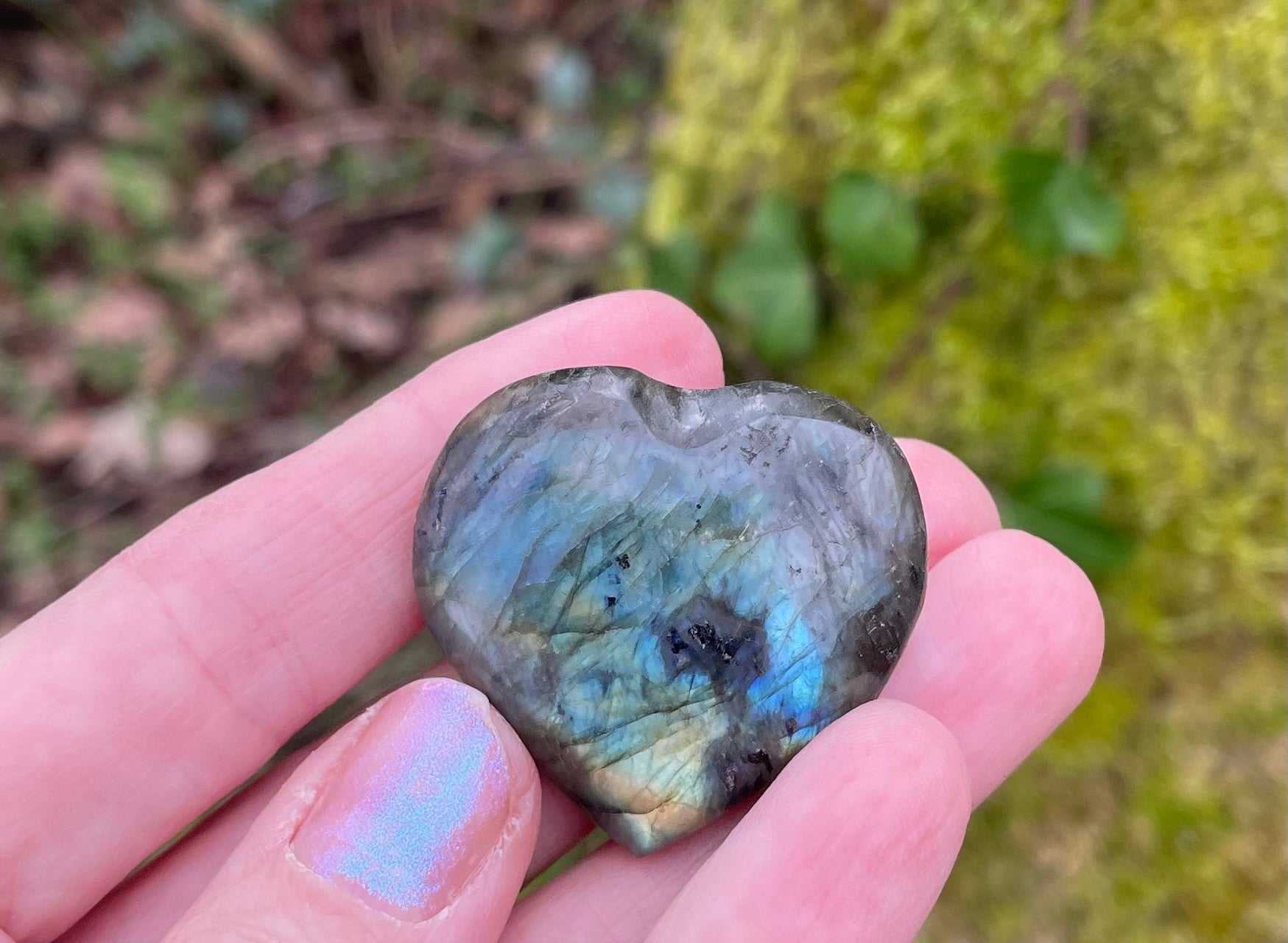 Heart shaped polished labradorite photographed in models hand in the woods