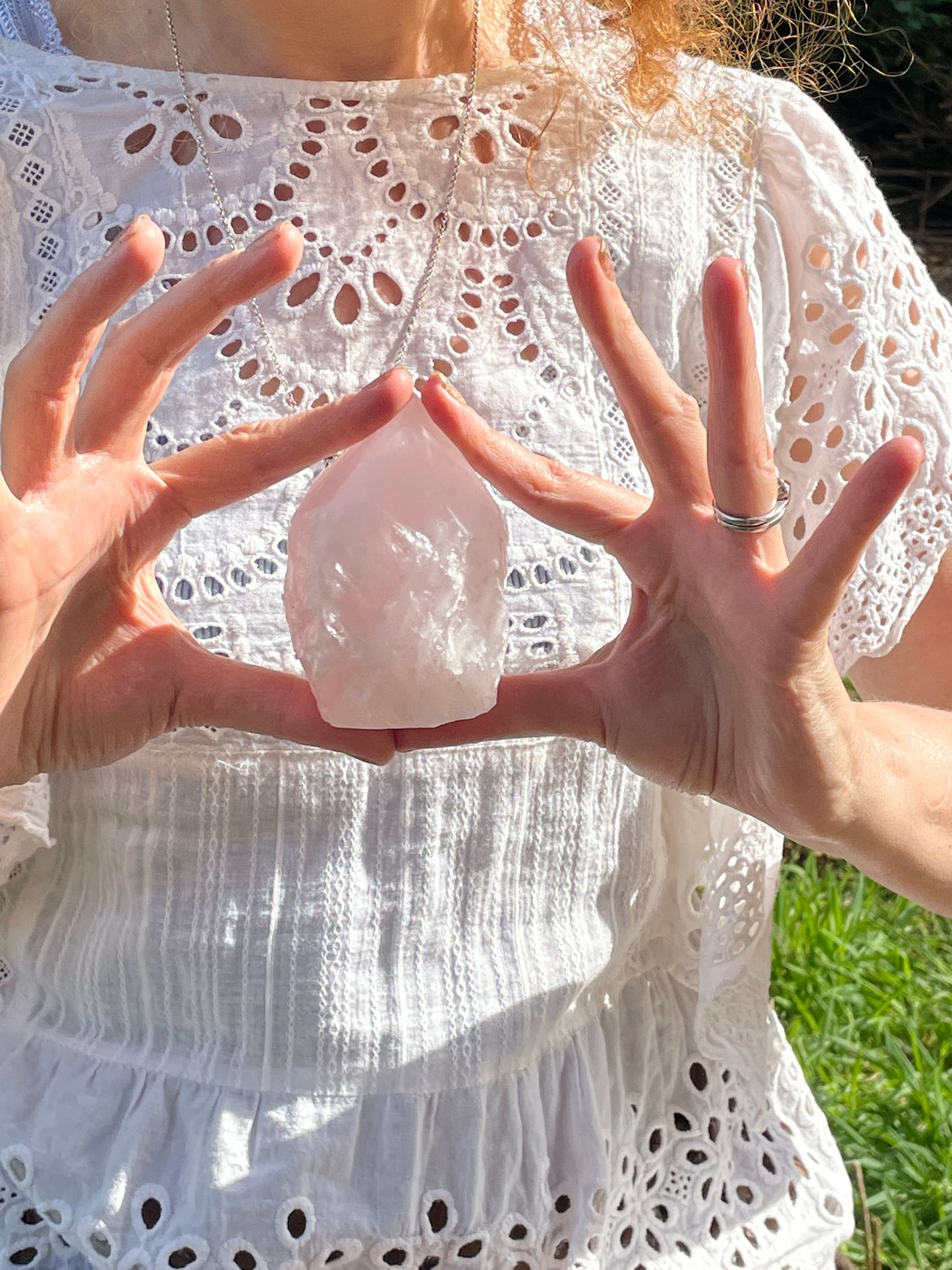 Soft pink rose quartz six sided pointed generator held in a model's hands showing the size of the crystal. She is wearing a white lace top.