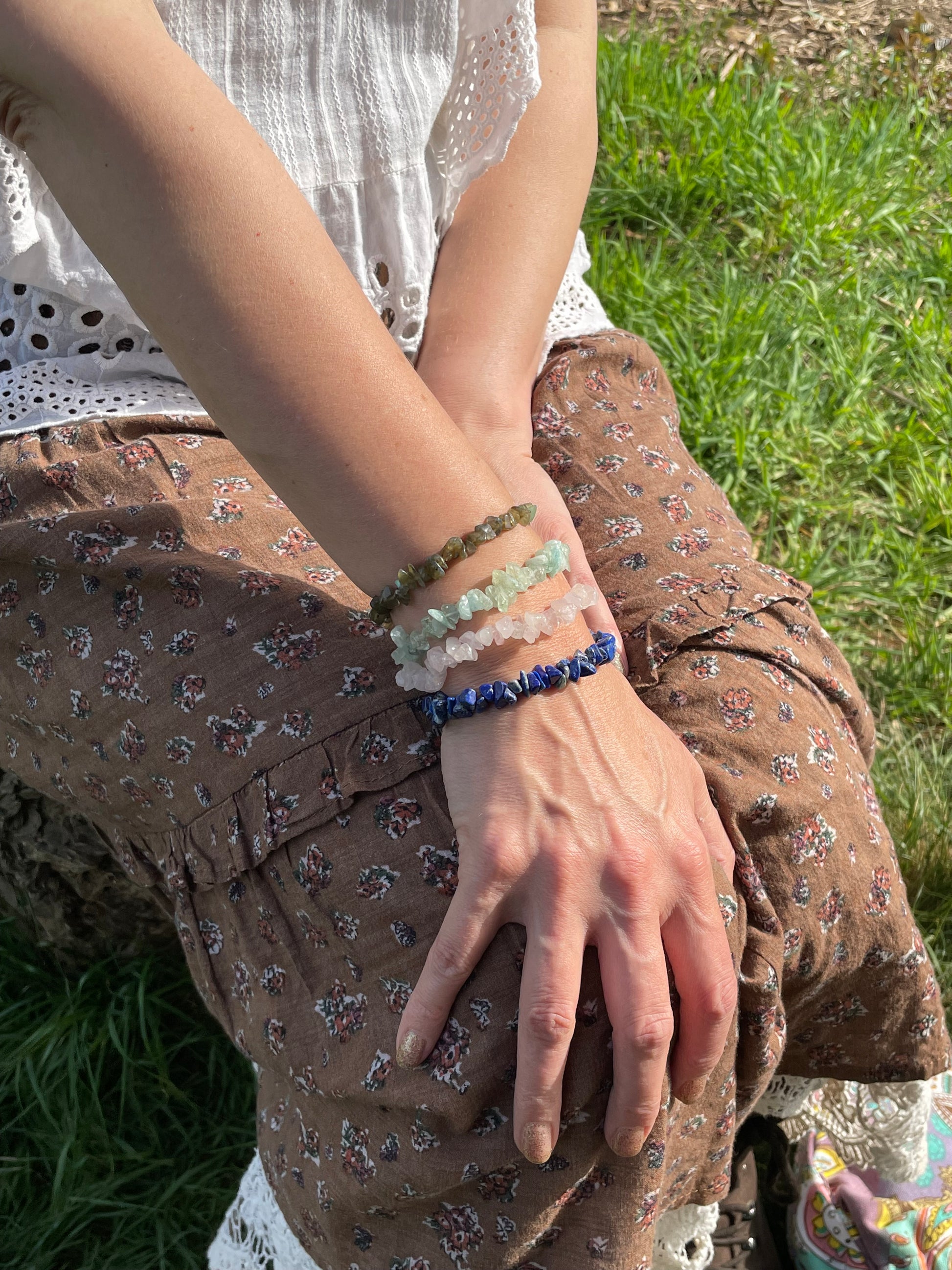 Model sitting in the woods wearing a few coloured crystal chip bracelets.