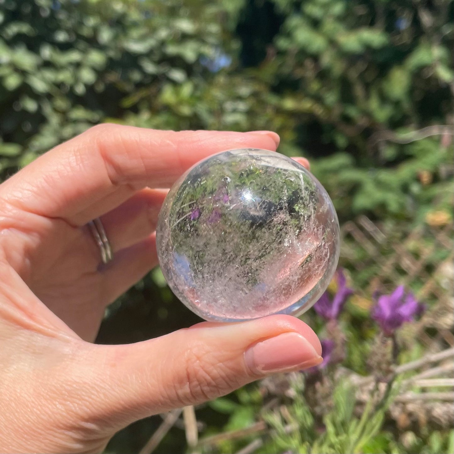 Clear quartz ball shown with sunbeams in a model's hand in forest background.