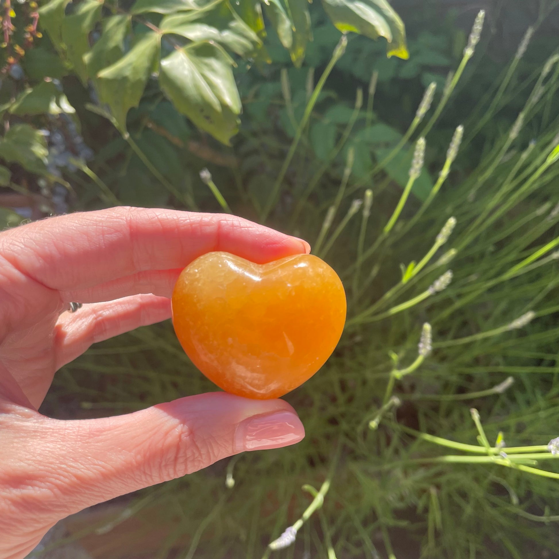 Bright orange smooth carved heart crystal held in a model's hand in the woods.