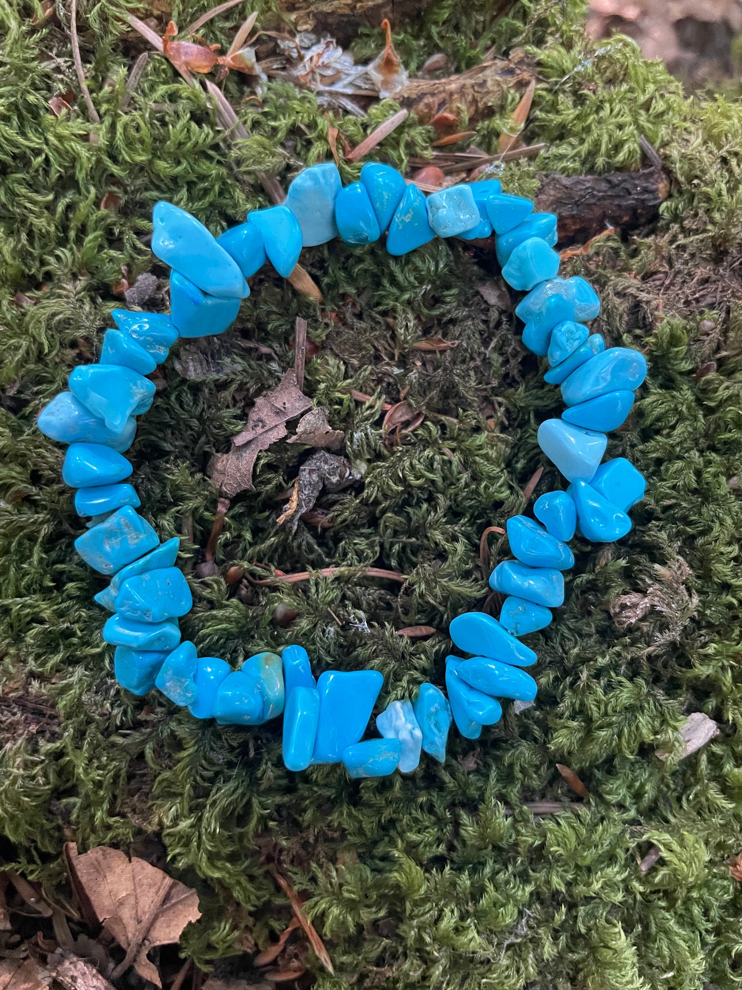 Deep turquoise blue crystal chip bracelet circular in shape sitting on moss.