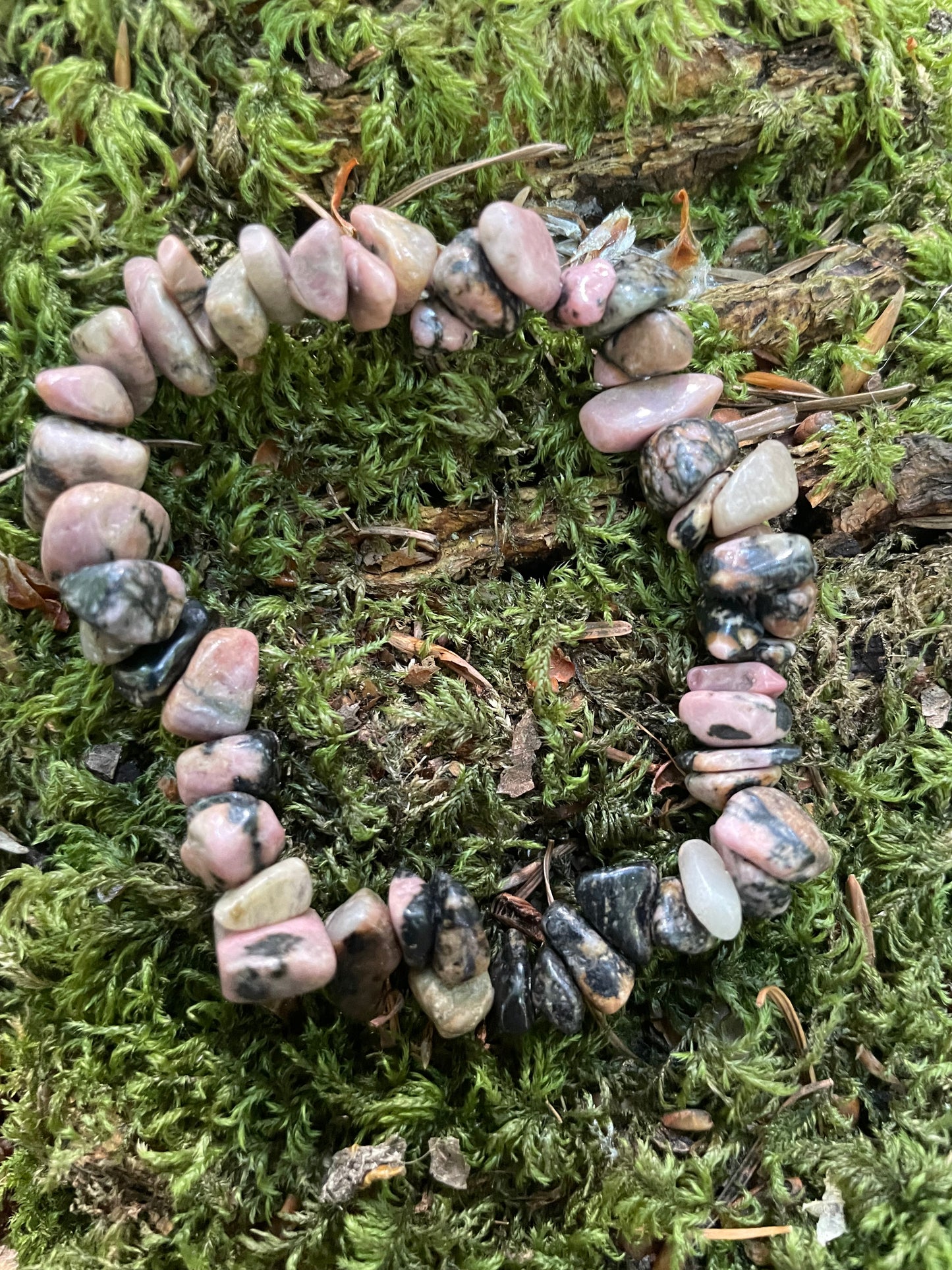 Pink and black mottled small crystal chip elasticated bracelet shown on moss.