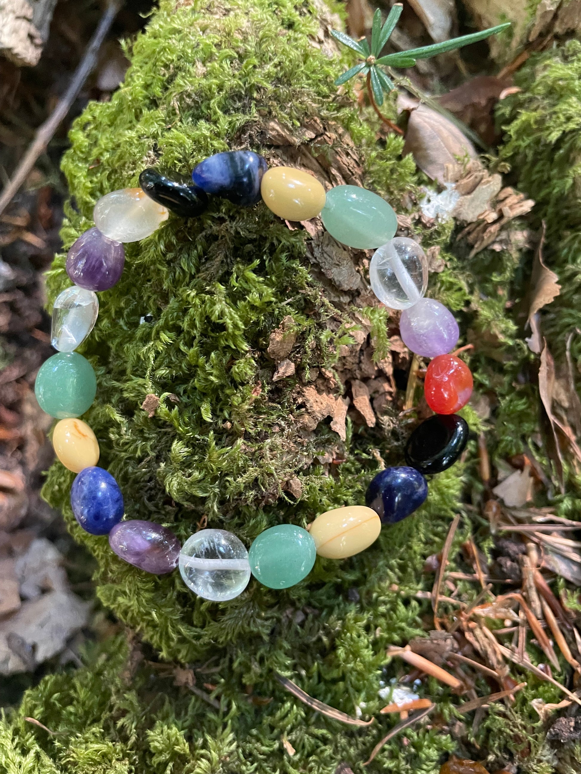 Multi -coloured tumble stone crystal bracelet displayed on moss.