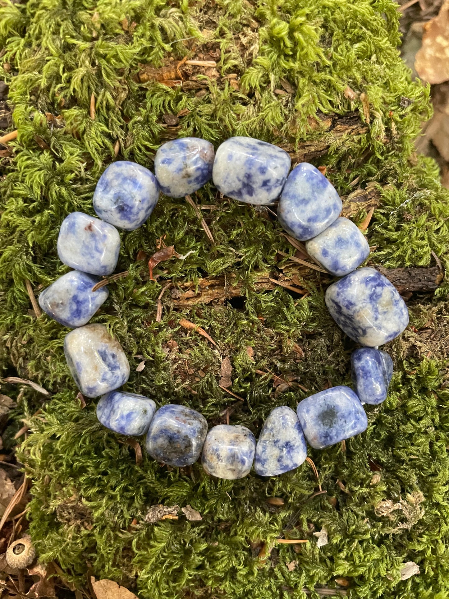 A blue and white little tumble stone crystal elasticated bracelet displayed on moss.