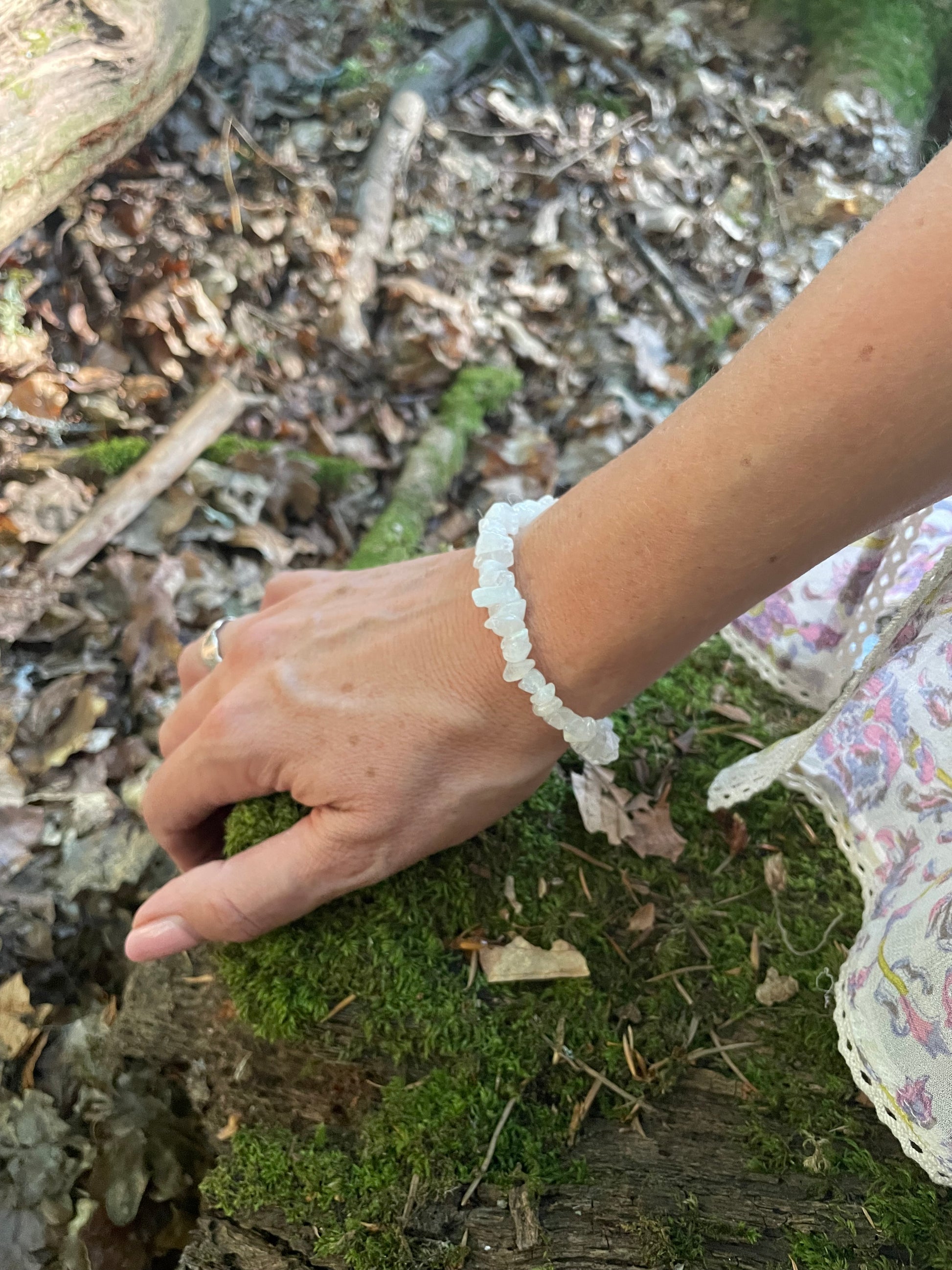 Pretty delicate white crystal bracelet made up of tiny chips on elastic. Shown on a models wrist with part of her sleeve showing in wooded background.