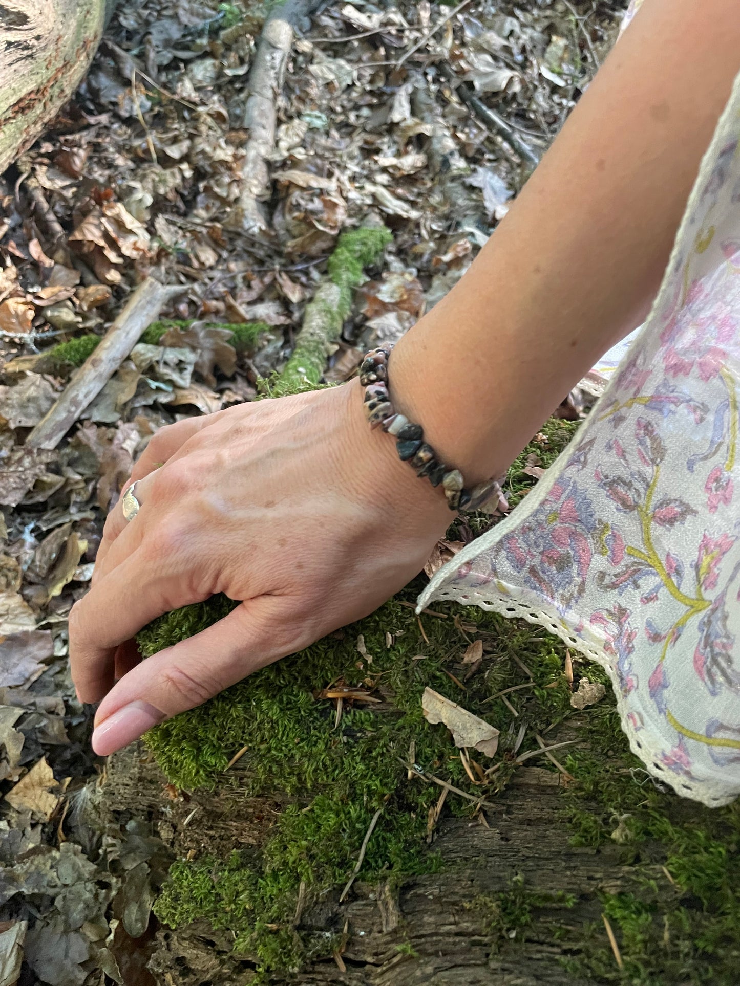 Pink and black mottled small crystal chip elasticated bracelet shown on a model's wrist with part of her floaty sleeve showing in forest background.