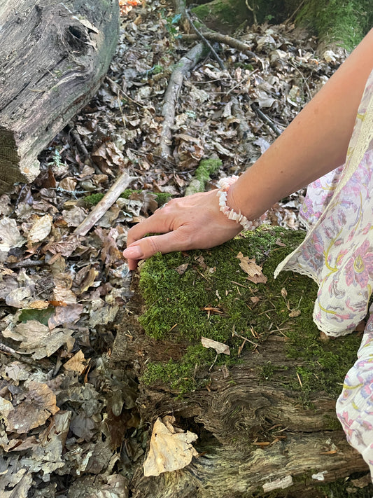 Pretty pastel pink crystal chip elasticated bracelet shown on a model's wrist with a part of her sleeve showing pictured in the woods.