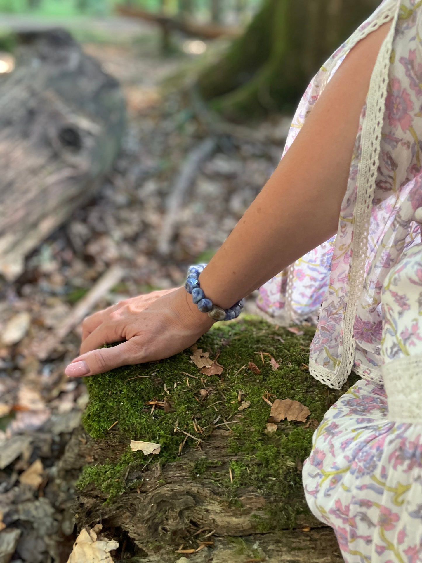 A model wearing a blue and white little tumble stone crystal elasticated bracelet. She is in the woods.