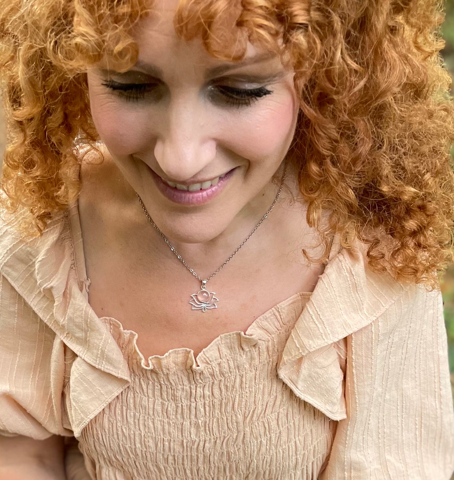 Silver plated lotus flower shaped pendant with a rose quartz embedded. It is on a chain worn around models neck. She is wearing a pink shirred dress.